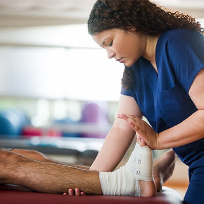 A female occupational therapist holding leg and foot of a male patient with a bandage in his ankle.